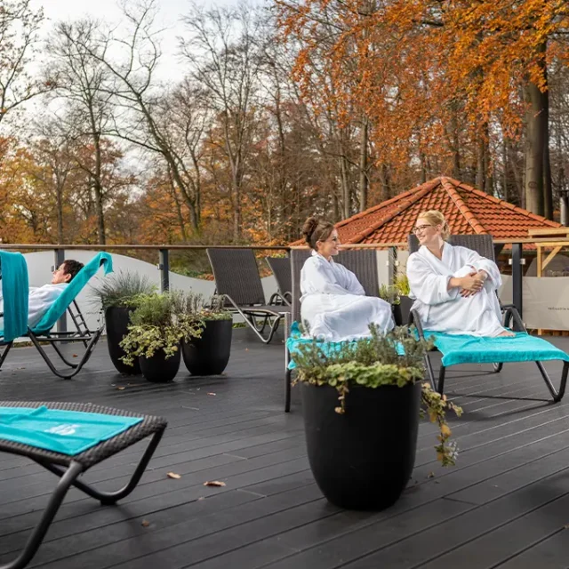 zwei Frauen sitzen draußen auf zwei Liegen im Bademantel